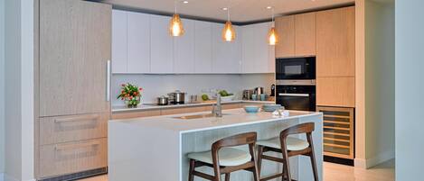 Una cocina moderna con una isla central, taburetes de bar, iluminación colgante y electrodomésticos integrados.