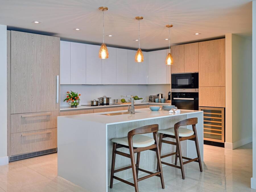 A modern kitchen with a central island, bar stools, pendant lighting, and built-in appliances.