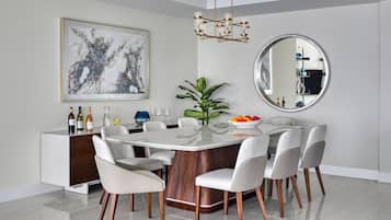 A modern dining room with a round table, white chairs, a wooden cabinet, a large abstract painting, a mirror, and a potted plant.