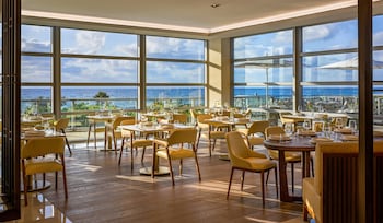 Enjoy a panoramic ocean view from the spacious dining area with large windows and round tables for guests. at Amrit Ocean Resort and Residences - Singer Island