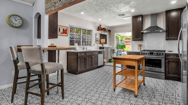A kitchen with a central island, dark wooden cabinets, a stainless steel stove, and a clock on the wall.