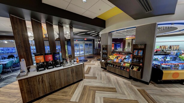 Un café moderne avec un comptoir en bois, des machines à café et un présentoir où sont exposés des en-cas et des boissons.