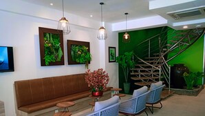 A modern lobby with a brown leather sofa, wicker chairs, a coffee table with a floral centerpiece, and a green wall with a spiral staircase. - H Boutique Hotel Xplorer Loke Yew (Kuala Lumpur)