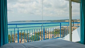 A room with a large window overlooking a beach and ocean, featuring a balcony with blue railings. - Yong Wong Hostel (Hengchun)