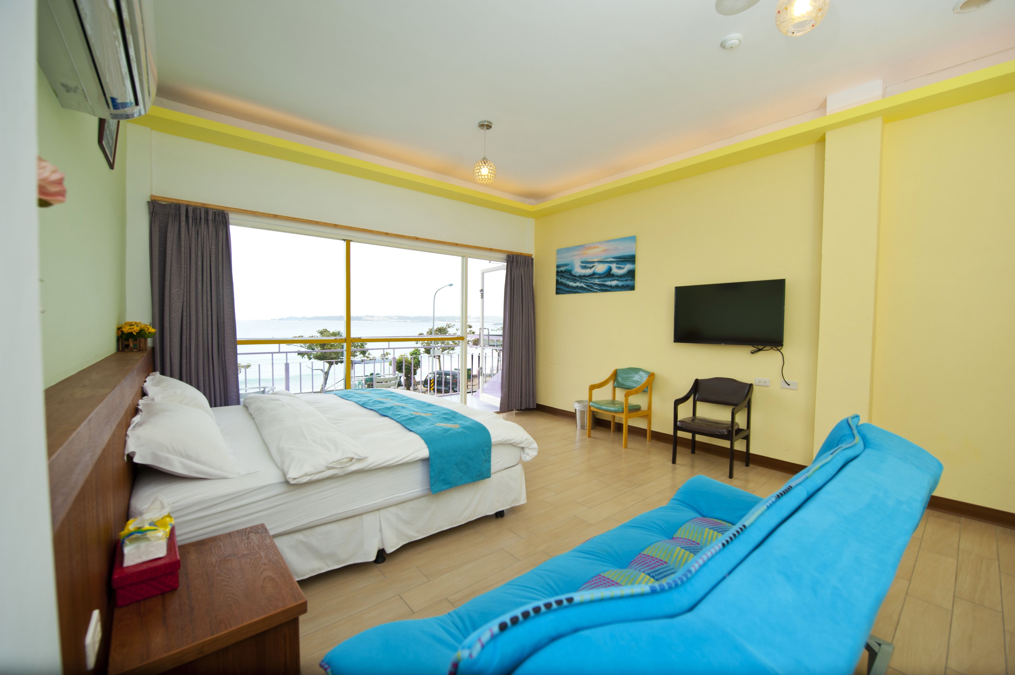 Habitación de hotel con cama, un sofá azul, televisión y balcón con vistas.
