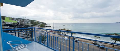 A balcony with a view of the sea, a road with cars, and a blue railing.