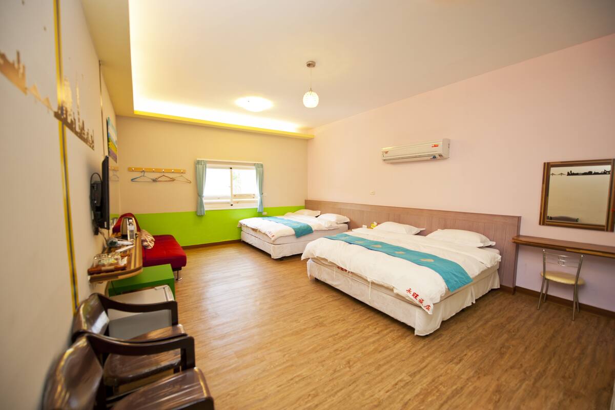 A hotel room with two beds, a desk, a chair, a mirror, and a window.