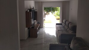 Ein Wohnzimmer mit einer Couch, einem Fernseher und Blick auf einen Garten durch eine Glastür.