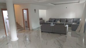 Ein geräumiges Wohnzimmer mit Marmorboden, einem grauen Ecksofa und einer Treppe, die in eine weitere Ebene führt.