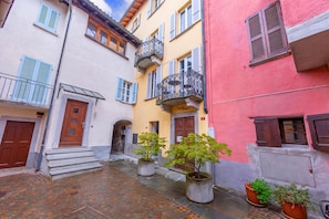 Une rue étroite bordée d’immeubles, avec une porte en bois et des plantes en pot.