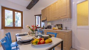 Une cuisine avec des meubles de rangement en bois, une table à manger avec des chaises et un panier de fruits.