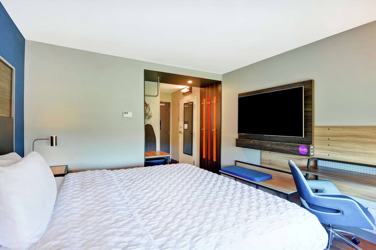 A hotel room with a large bed, a TV mounted on the wall, a desk, and a chair.