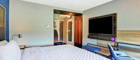 A hotel room with a large bed, a TV mounted on the wall, a desk, and a chair.