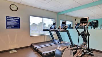 A fitness center with treadmills, an elliptical, and a stationary bike. There's a large window, a clock, and a sign with equipment usage instructions.