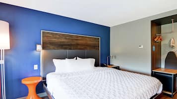 Una habitación de hotel moderna con una cama grande, un cabecero de madera, una mesita de noche naranja pequeña y un espejo con toallero.