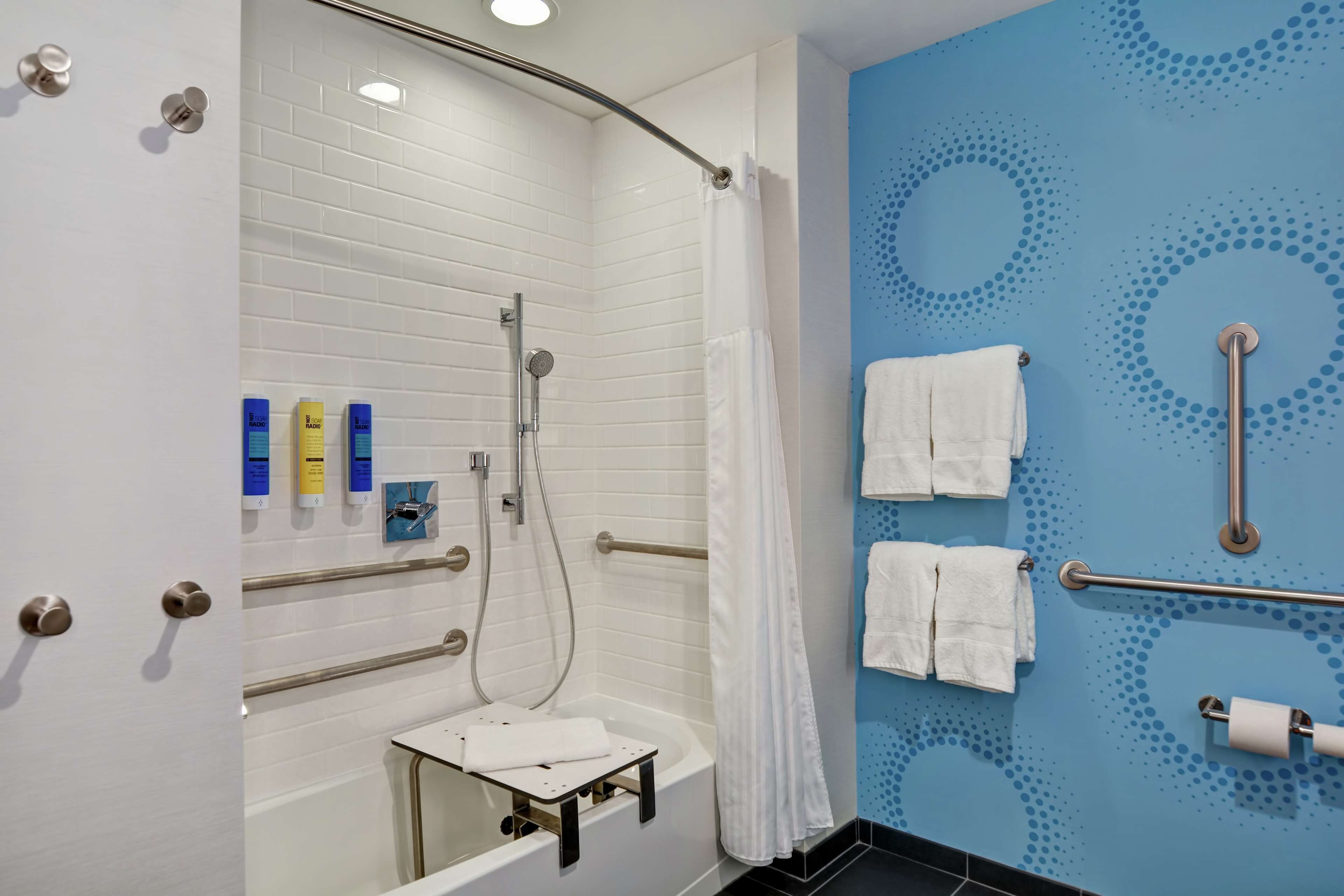 A modern bathroom with white tiles, a shower with a glass door, a bathtub, and a blue wall with a circular pattern.