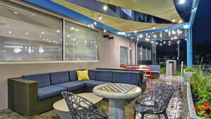 An outdoor seating area with a blue sofa, round table, and chairs, under a canopy with string lights. - Tru by Hilton Middletown (Middletown)