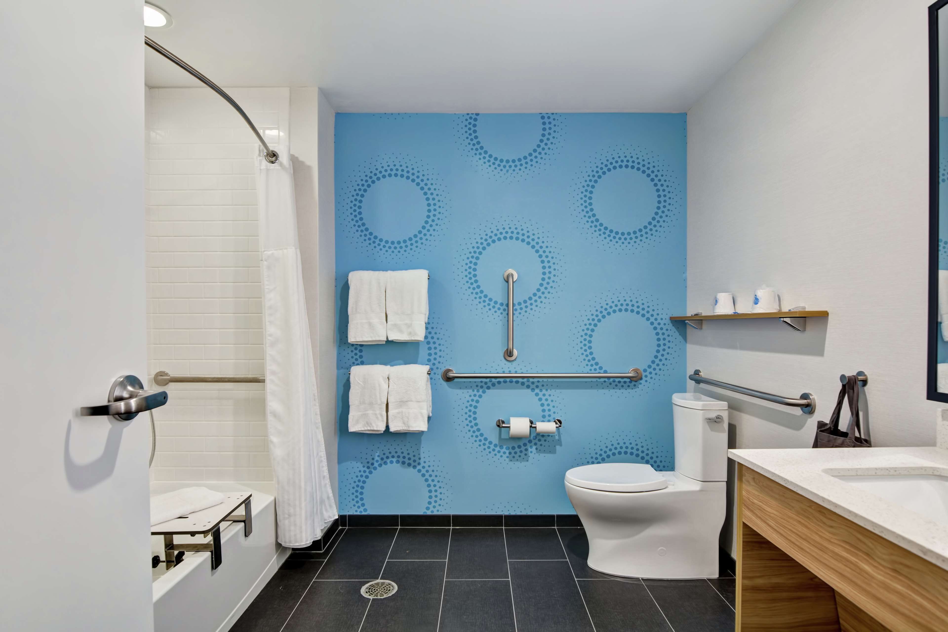 Une salle de bain moderne avec un mur à motifs bleus, des toilettes blanches, un espace douche et un meuble-lavabo avec un miroir.