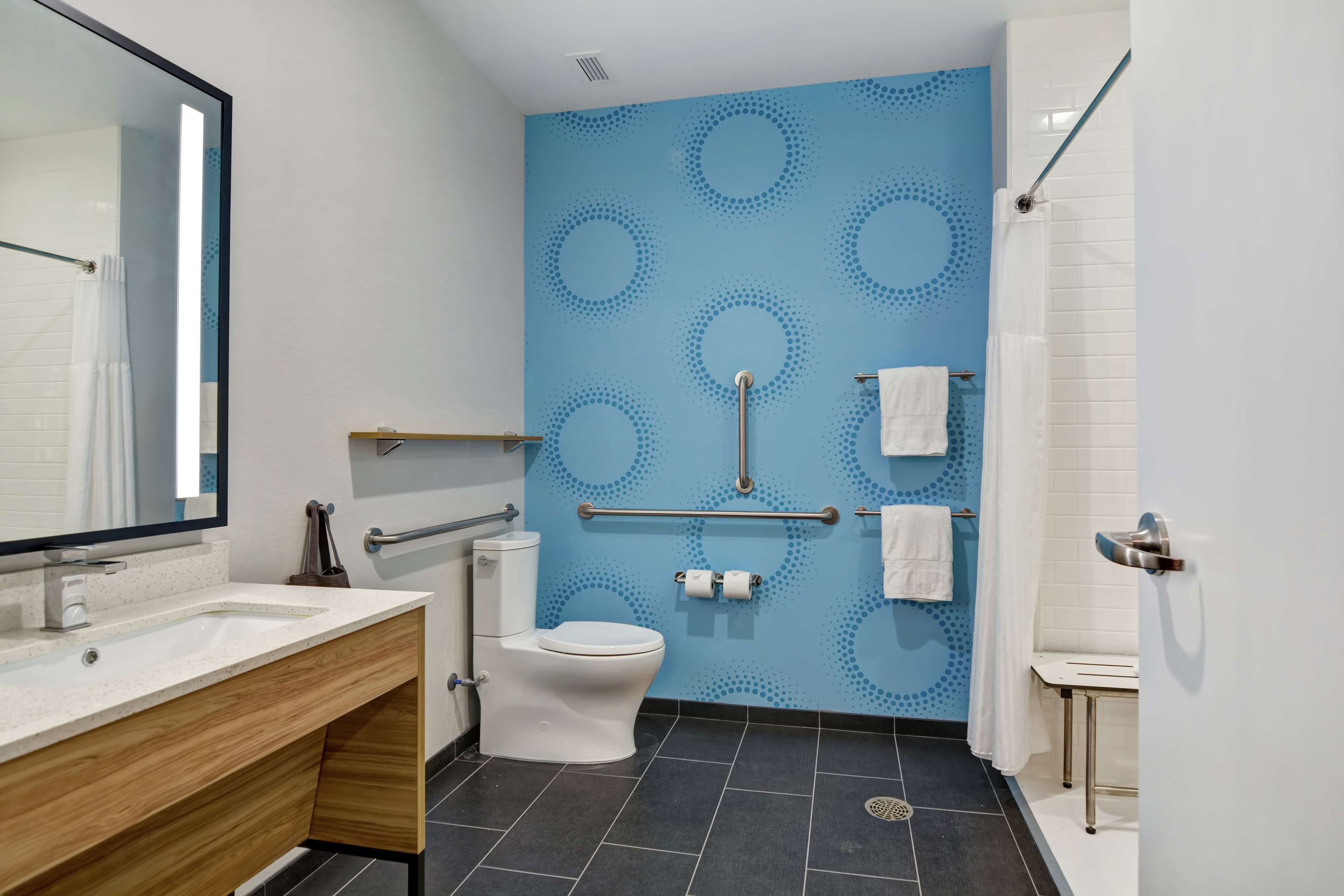 A modern bathroom with a blue patterned wall, a white toilet, a sink with a wooden vanity, and a shower area.