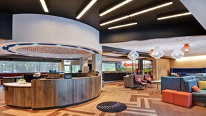 A modern reception area with a curved wooden counter, seating area with colorful cushions, and pendant lighting. - Tru by Hilton Middletown (Middletown)