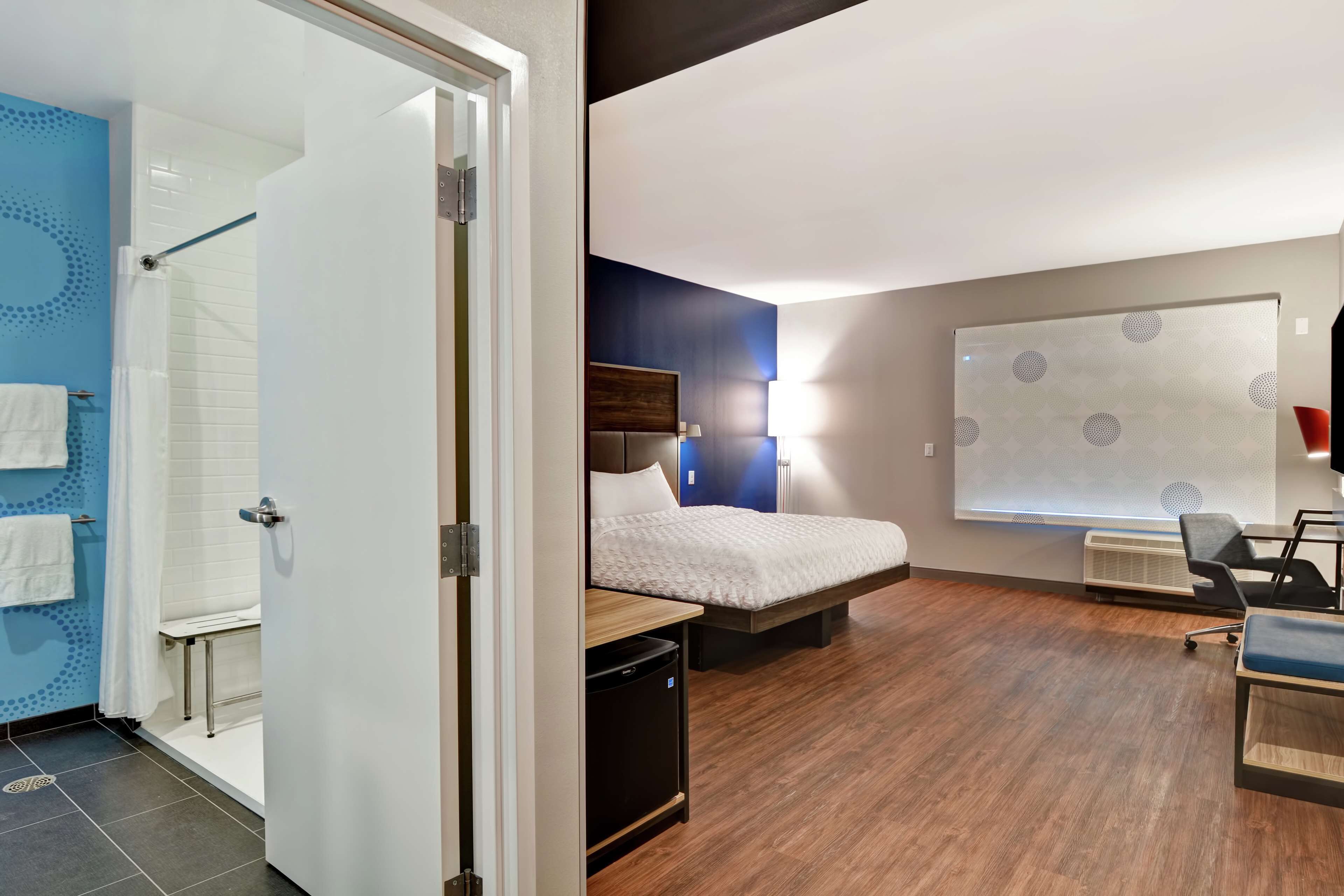 Hotelkamer met douche, bed, bureau en een projectiescherm.