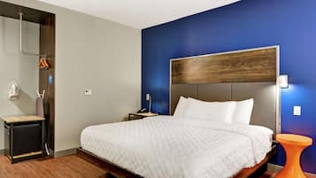 A modern hotel room with a large bed, a wooden headboard, a nightstand, a small table, and a unique orange stool.