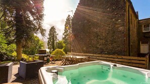 Ein Whirlpool in einem Garten mit Steinmauer, Gartenmöbeln und einem Grill.