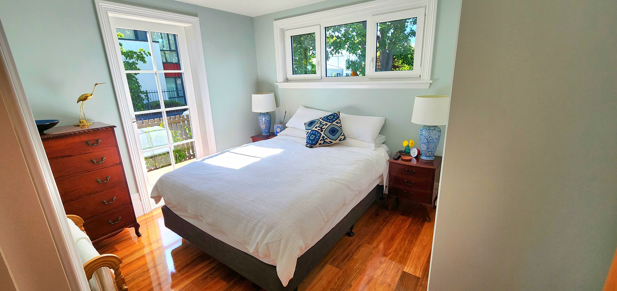 Une chambre à coucher comprenant un lit, une commode, deux tables de chevet et une fenêtre donnant sur un paysage verdoyant.