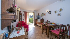 Un comedor con mesa de madera, sillas y un sofá rojo. Hay una zona de cocina con armarios y un televisor.