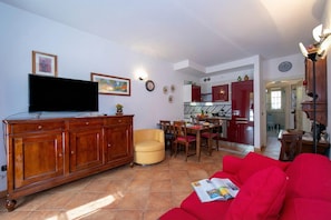 A living room with a red sofa, a television on a wooden cabinet, a dining area with chairs and a table, and a kitchen in the background. - Casa Emma with Pool, Sirmione, Italy (Sirmione)