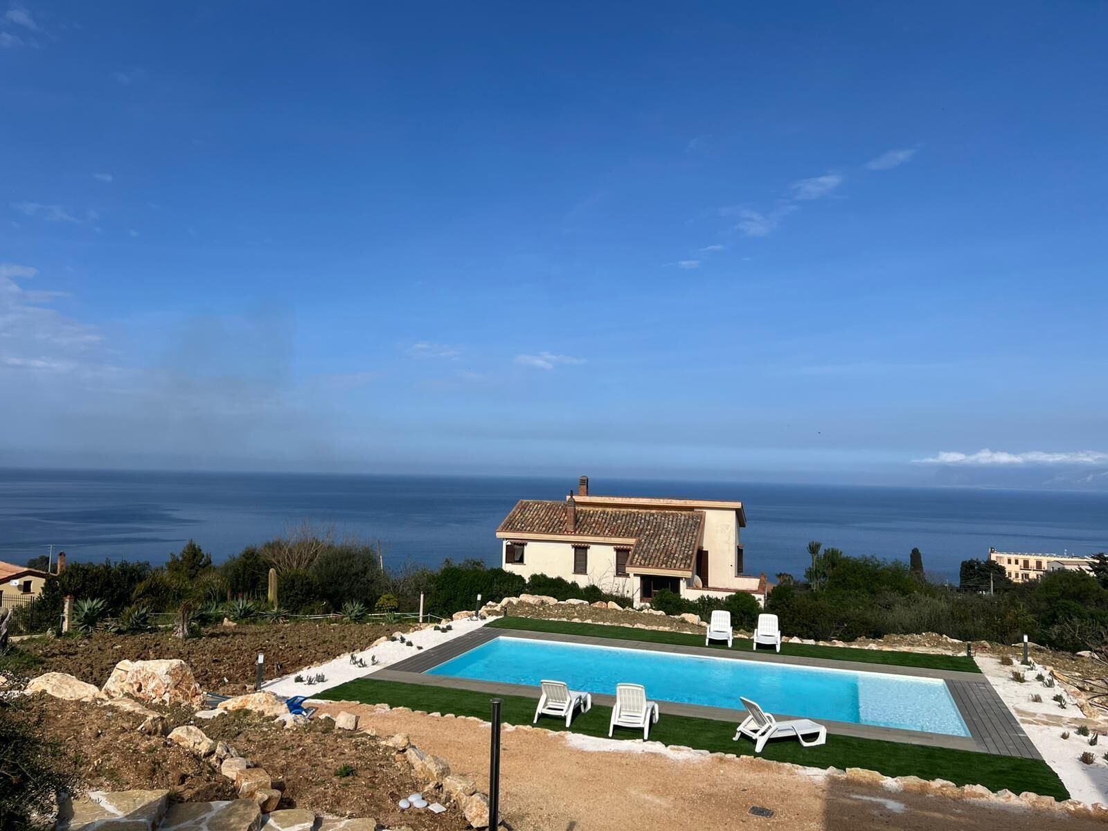 Une piscine avec des chaises longues, un bâtiment doté d’un toit en tuiles et une vue sur la mer.