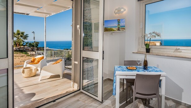 A balcony with a view of the sea, a dining table with a blue tablecloth, and a potted orchid.