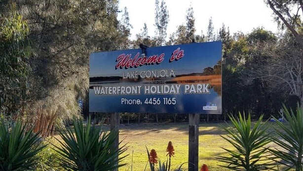En välkomstskylt för Waterfront Holiday Park, med en vacker utsikt över sjön.