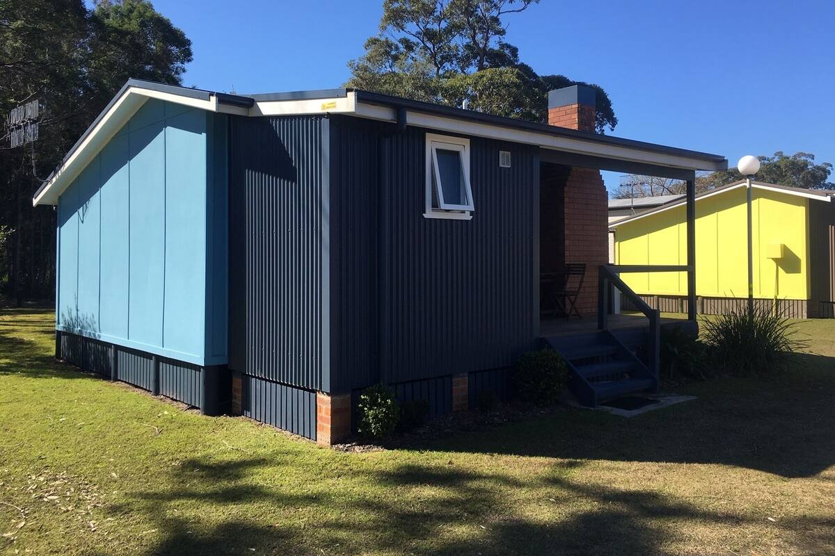 Een klein, laag gebouw met een donkerblauwe buitenkant en een geel gedeelte aan de rechterkant. Het heeft een klein raam en een deur, met een metselaarsschouw zichtbaar door het raam.