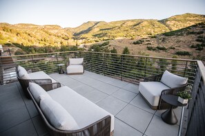Eine Terrasse mit einer Couch und Stühlen, einem kleinen Tisch und Blick auf eine gebirgige Landschaft.