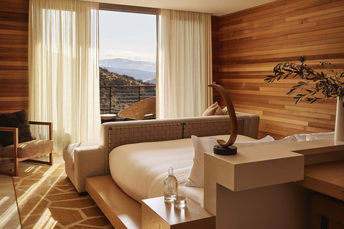A modern hotel room with a large bed, a seating area with a view, and a balcony with a railing.