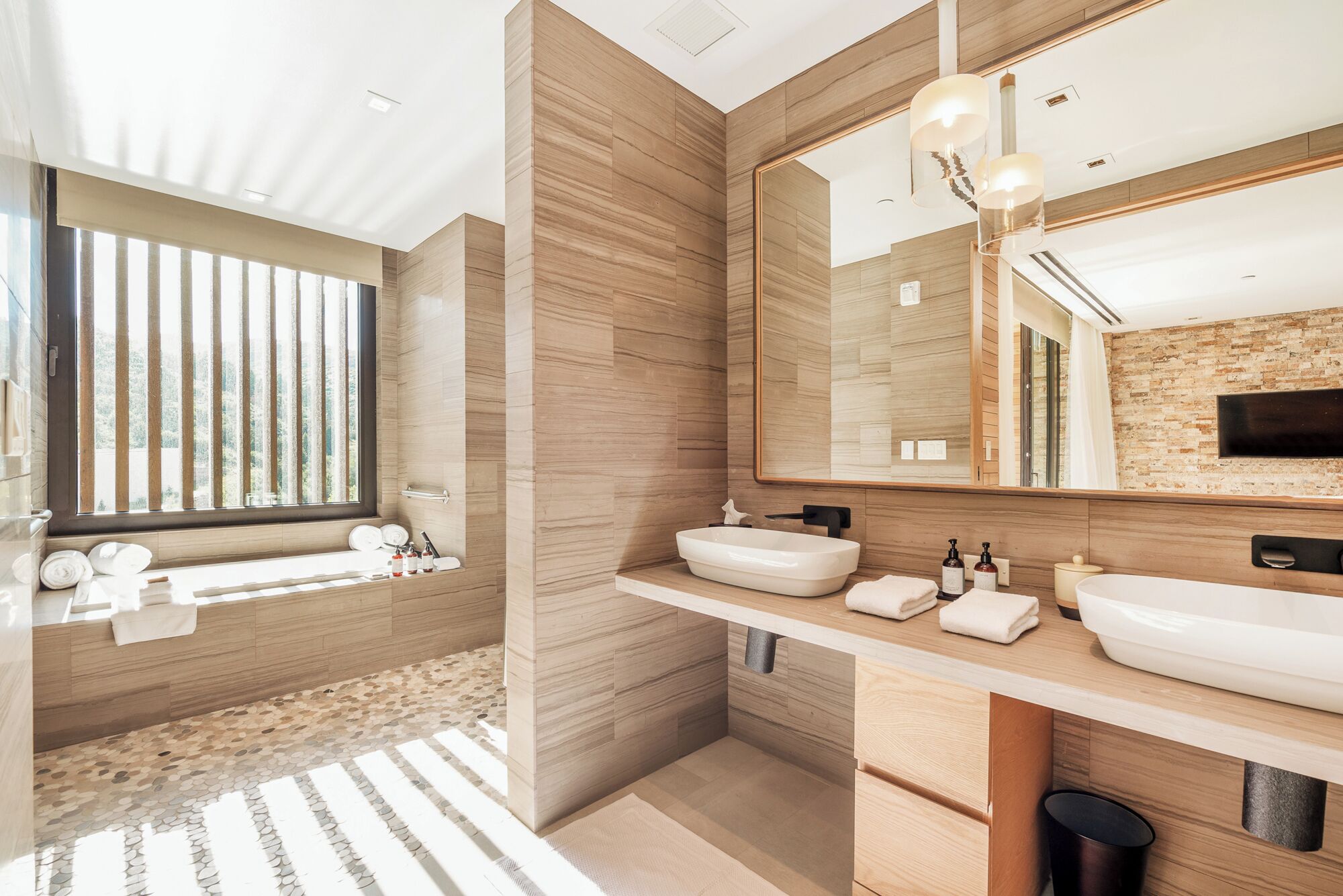 A modern bathroom with two sinks, a large mirror, and a window with vertical blinds.