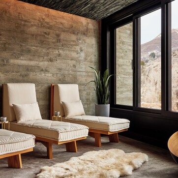 A modern room with three cushioned seating areas, a large wooden bowl, and a view of a mountainous landscape through large windows.