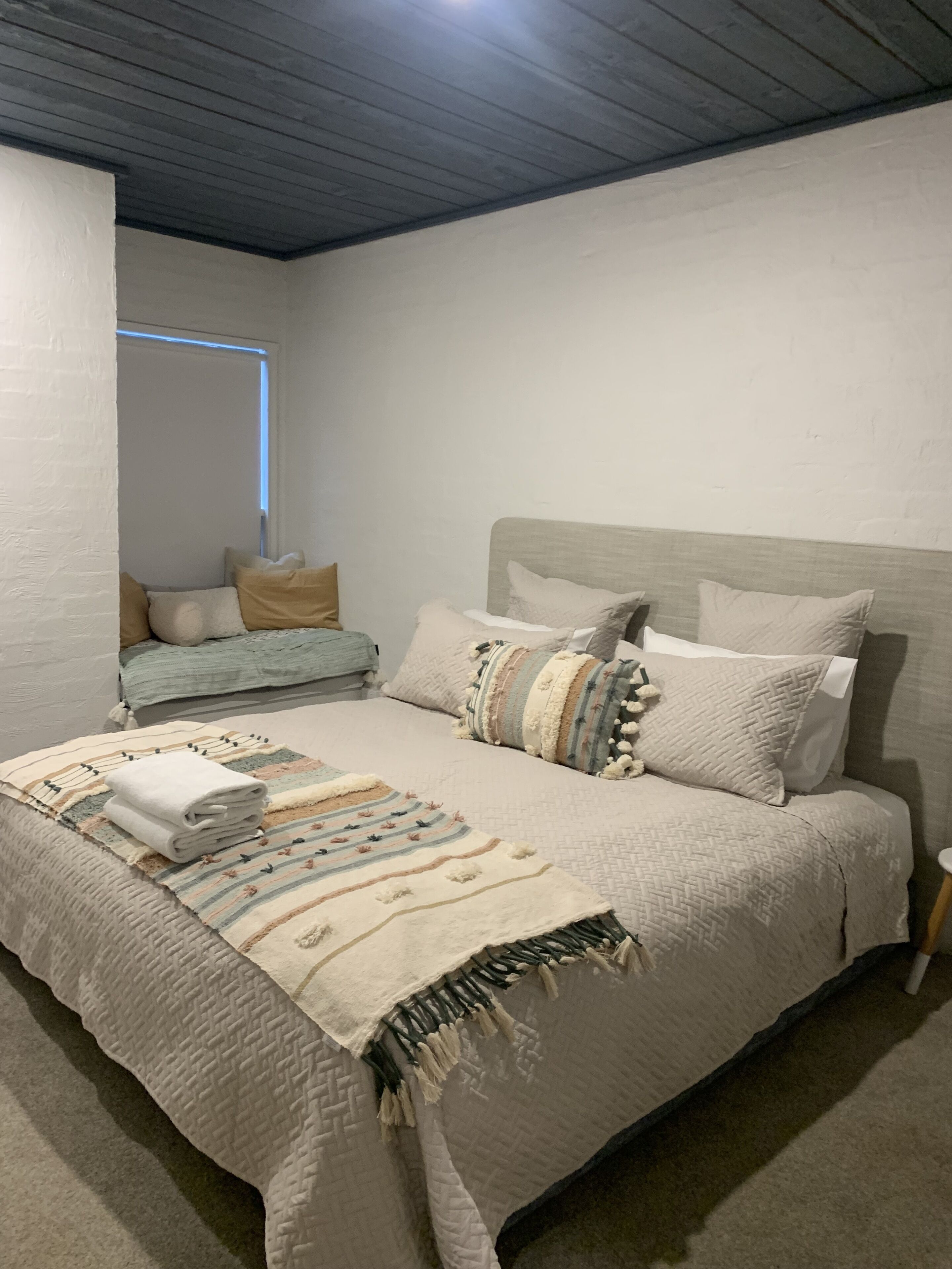 Een slaapkamer met een bed, kussens, een deken en een raam.