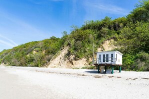 Ein Rettungsturm am sandigen Strand, im Hintergrund üppige Vegetation und ein klarer Himmel.