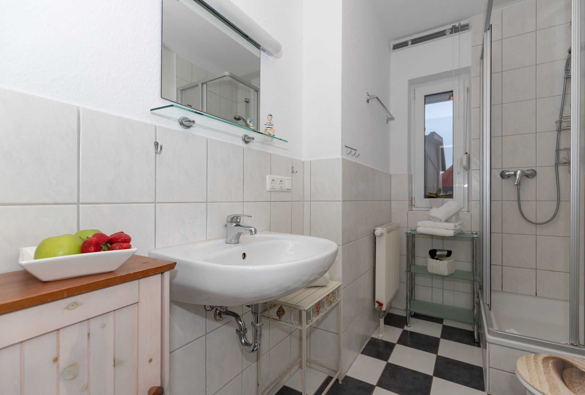 A bathroom with a white sink, mirror, and shower. There is a bowl of fruit on the counter.