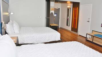 A hotel room with two beds, a wooden floor, a mirror, and a door with orange curtains.