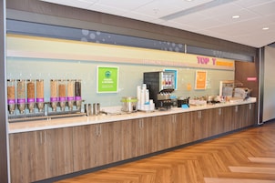 Una estación para desayuno con dispensadores de yogur y avena, una máquina de café y un cartel que anuncia 'Top T Breakfast'.