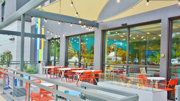 Een terras met oranje stoelen en tafels, een glazen balustrade en uitzicht op de stad door grote ramen.