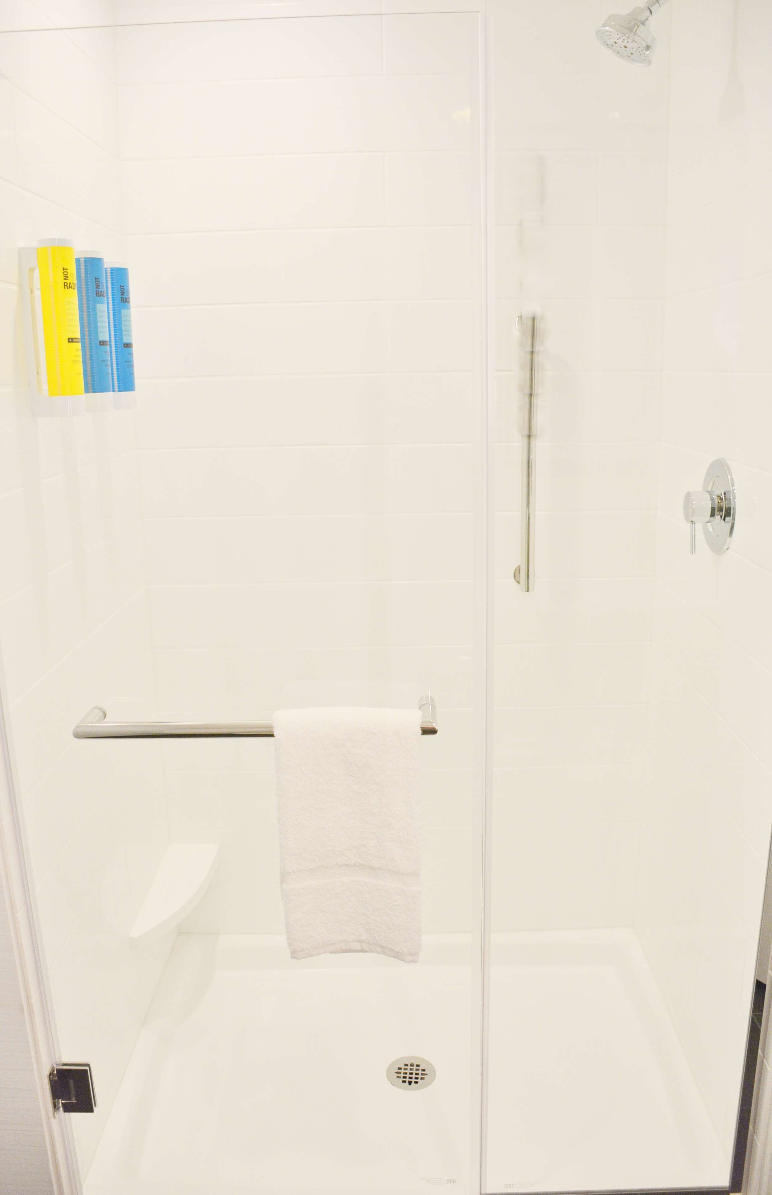Une douche fermée par des parois de verre, avec une serviette blanche suspendue à un porte-serviettes, un pommeau de douche et un drain.
