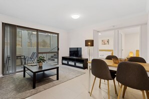 A modern living room with a TV, dining table, chairs, and a large window.
