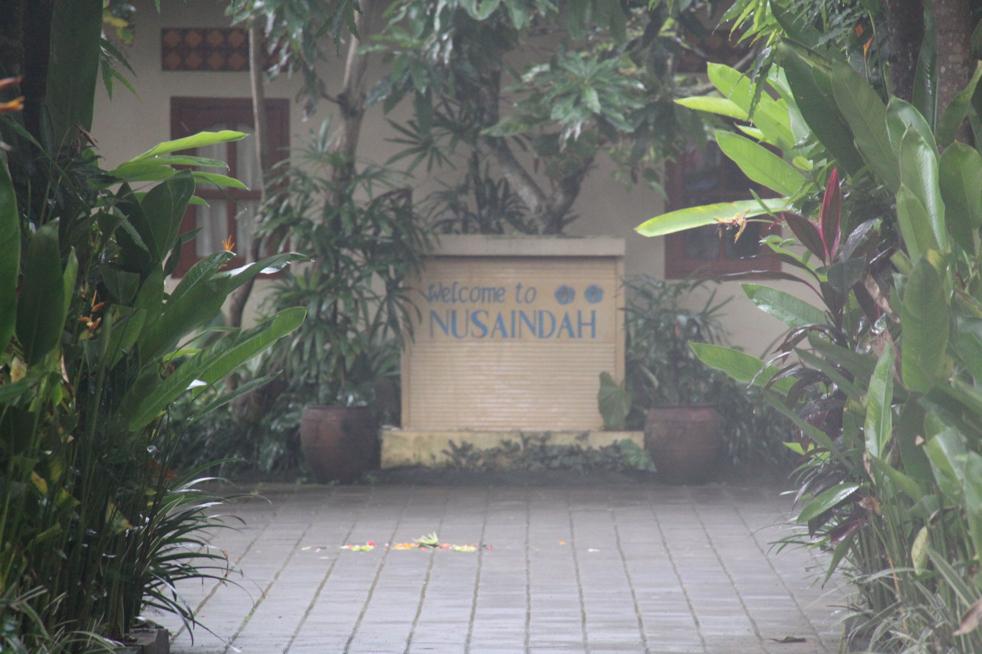 A welcome sign at the entrance of a building surrounded by lush greenery.