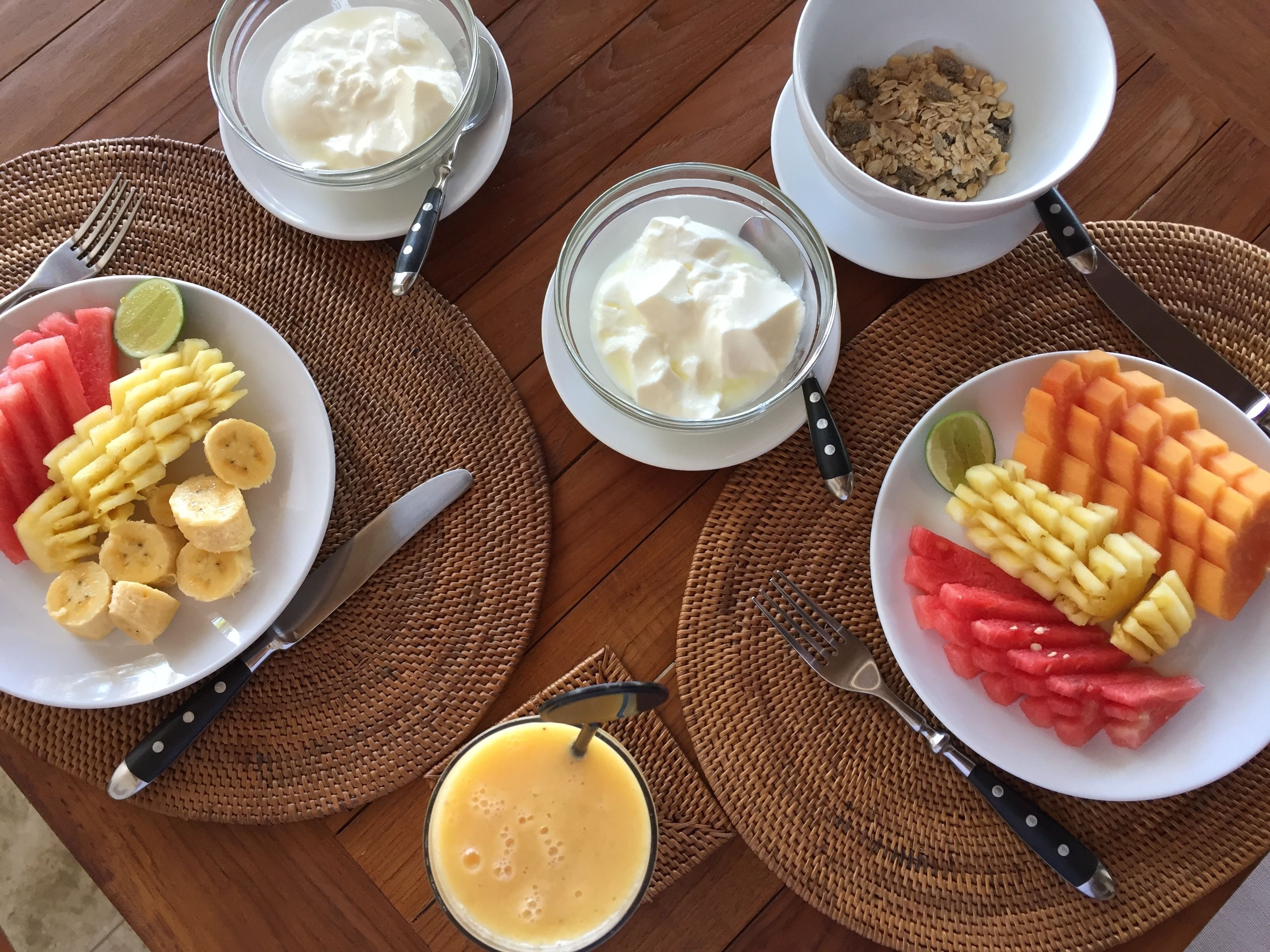 A table with bowls of yogurt, cereal, and fruit, and a glass of orange juice.