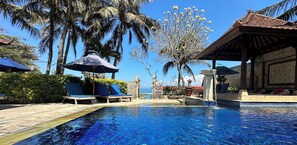 Una piscina de resort con agua cristalina azul, rodeada de palmeras y sillas de descanso.