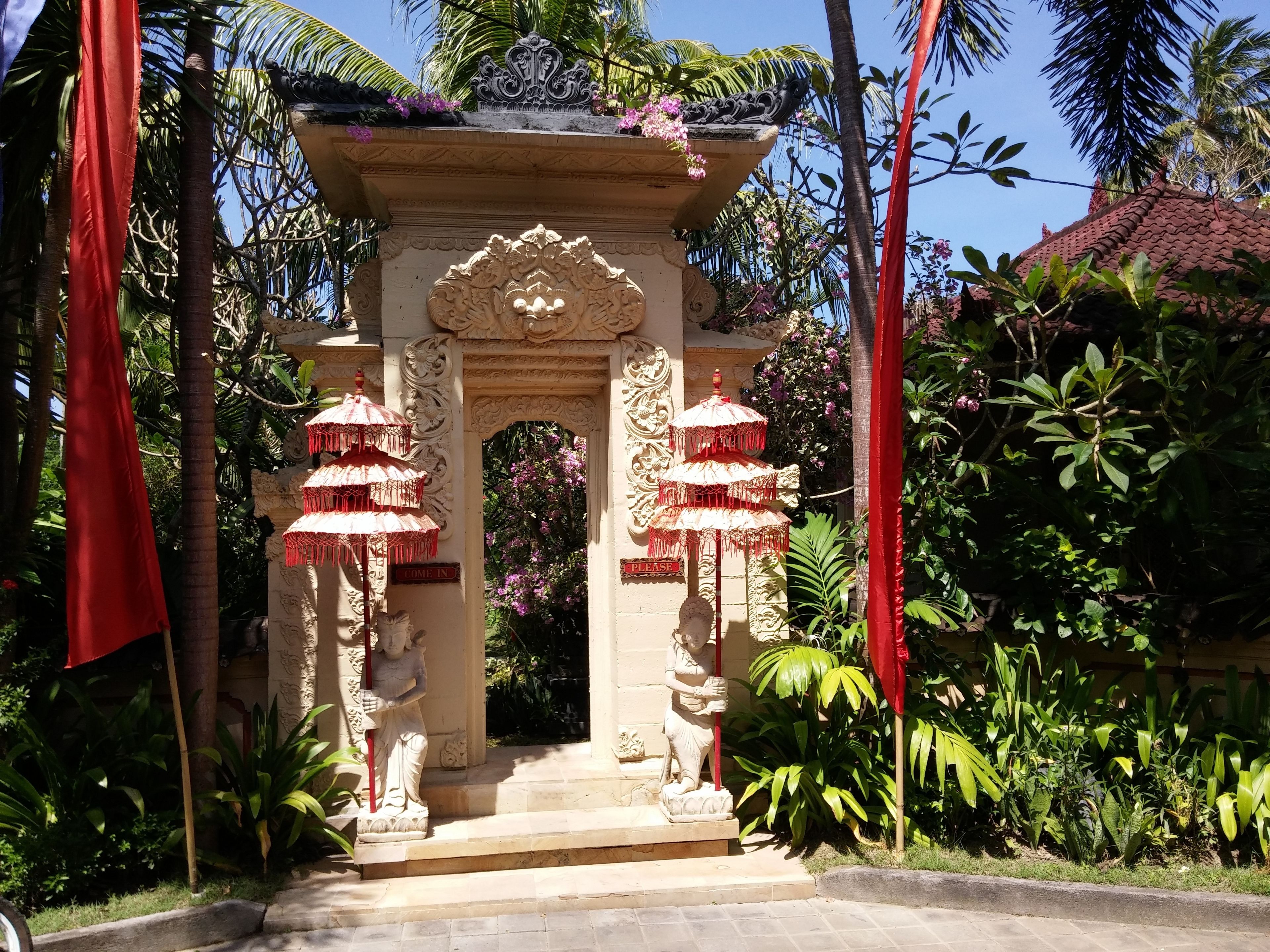 Una entrada ornamentada con dos sombrillas rojas, un arco central y una estatua a cada lado.